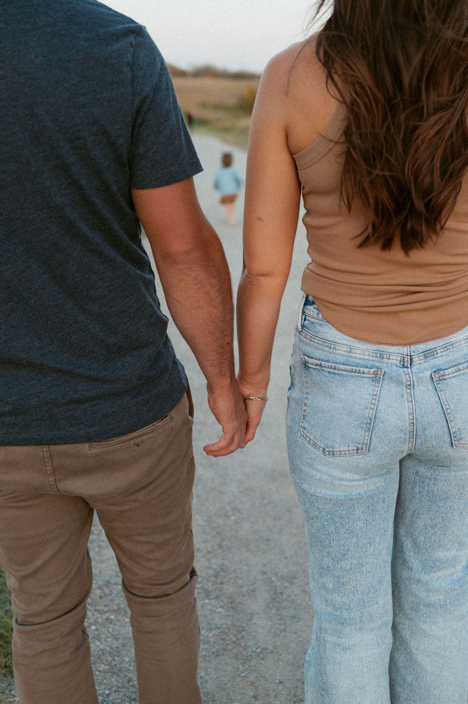A couple holding hands while walking together, wearing casual clothing of jeans and t-shirts on a dirt path.