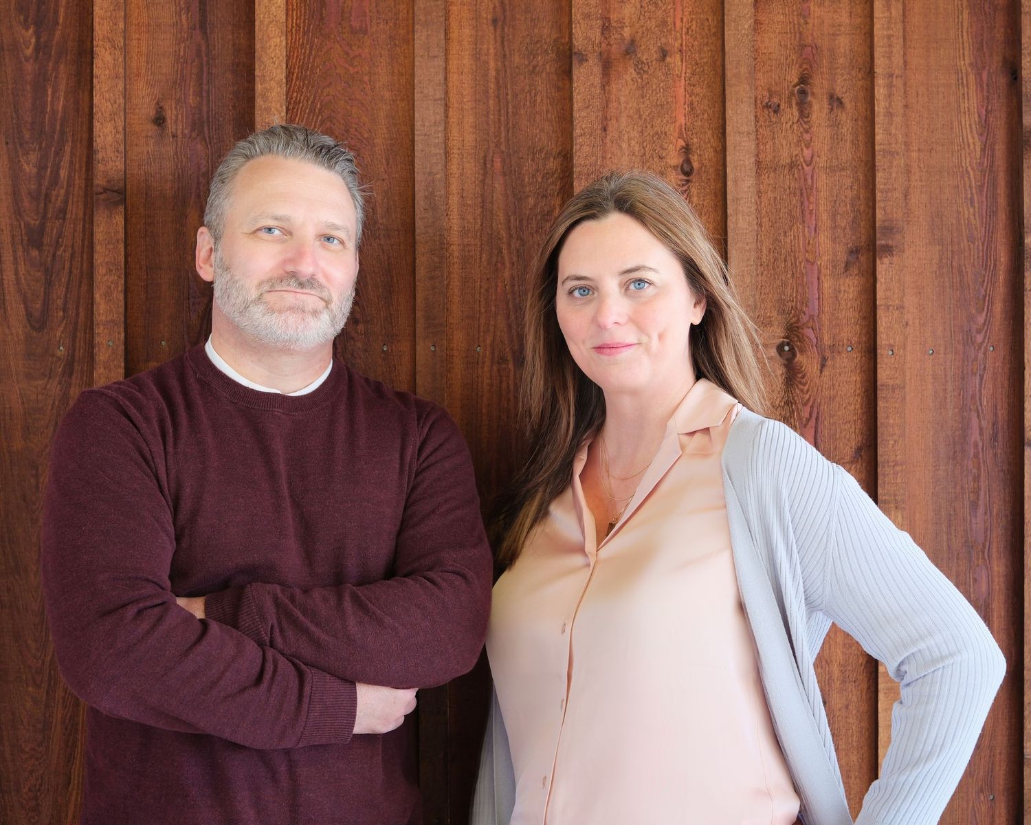 Two professionals in casual attire posed against a wooden wall background.