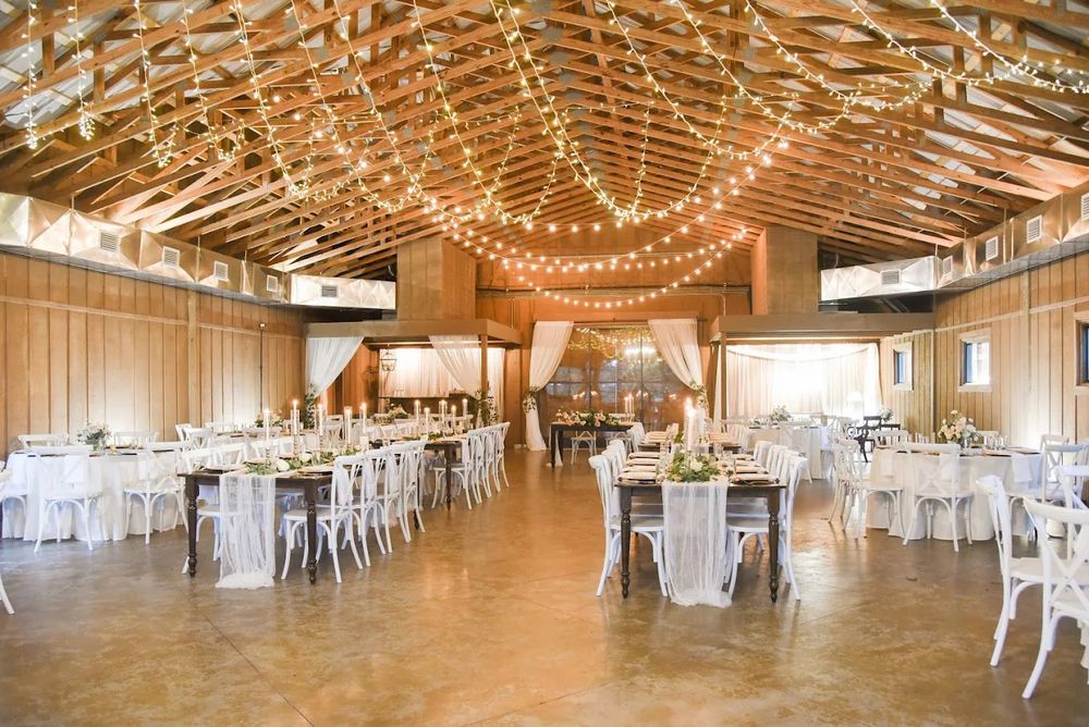 Rustic barn wedding reception venue with string lights, white chairs and round tables set for an elegant celebration.