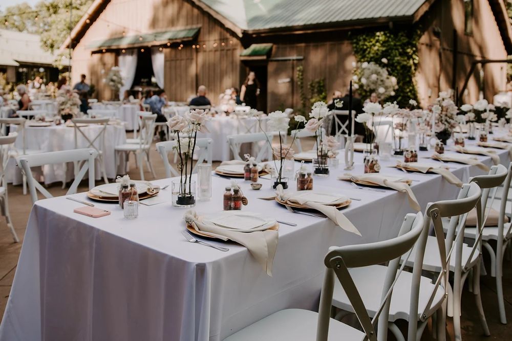 Elegant rustic wedding reception venue with white linens and place settings arranged at round tables.