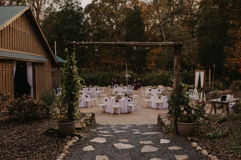 Rustic barn wedding venue with outdoor reception area featuring white tables and chairs set on stone pathway during autumn.