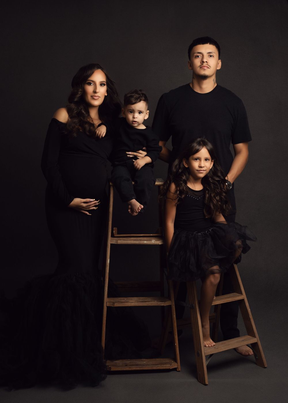 Dramatic black and white studio portraits of family members sitting on wooden chairs against dark background.