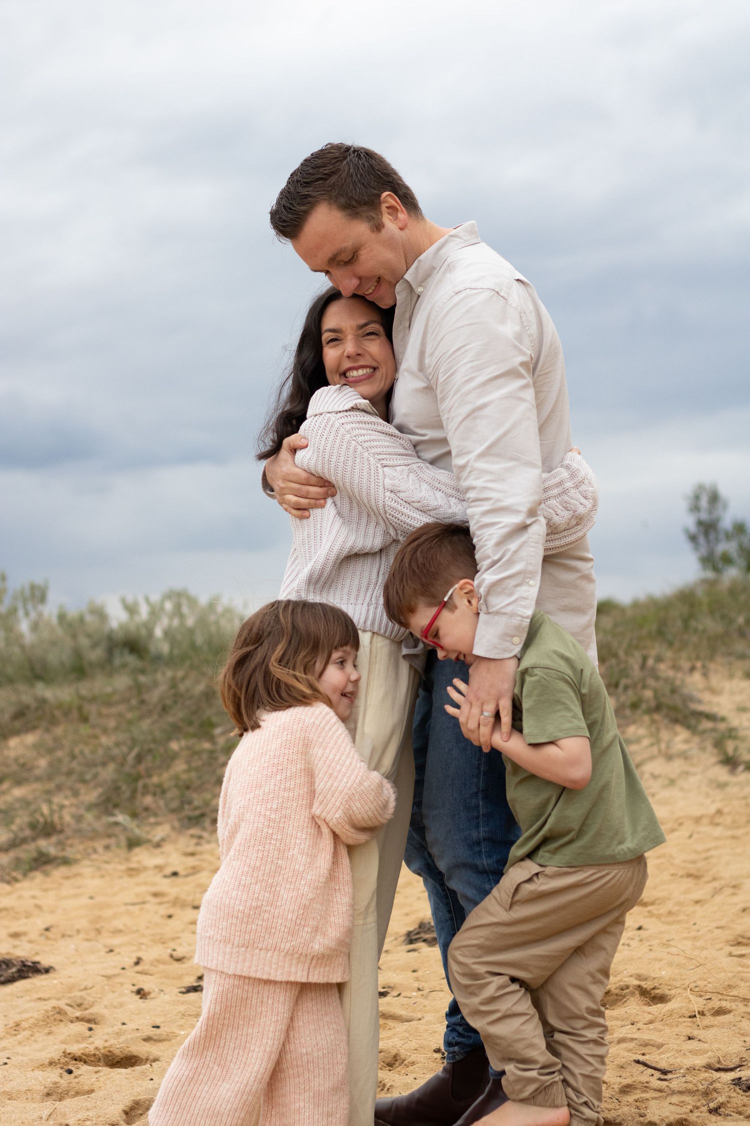 A tender family embrace on a sandy beach with stormy clouds in the background.