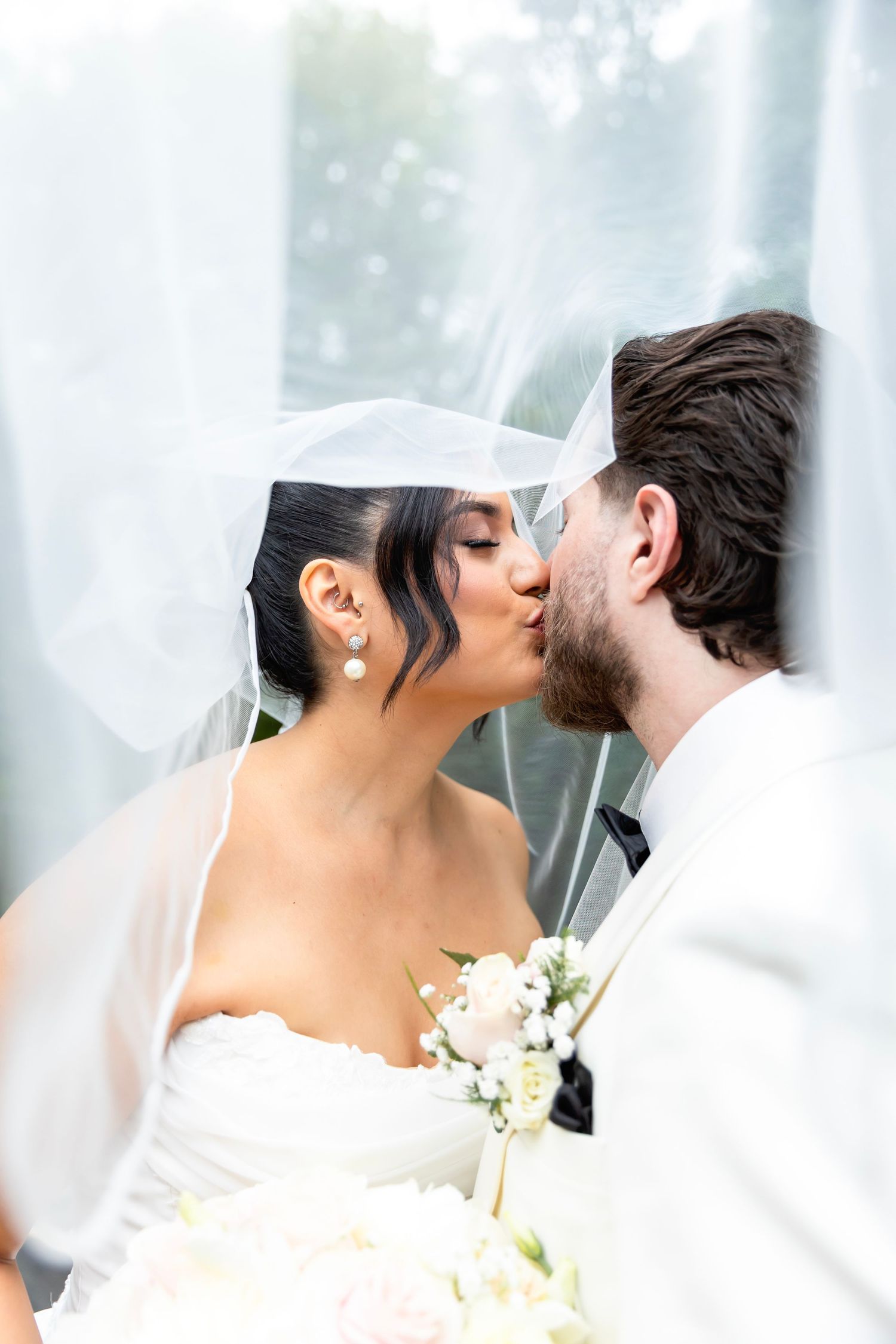 A romantic wedding moment captured under a flowing veil as the couple shares their first kiss.