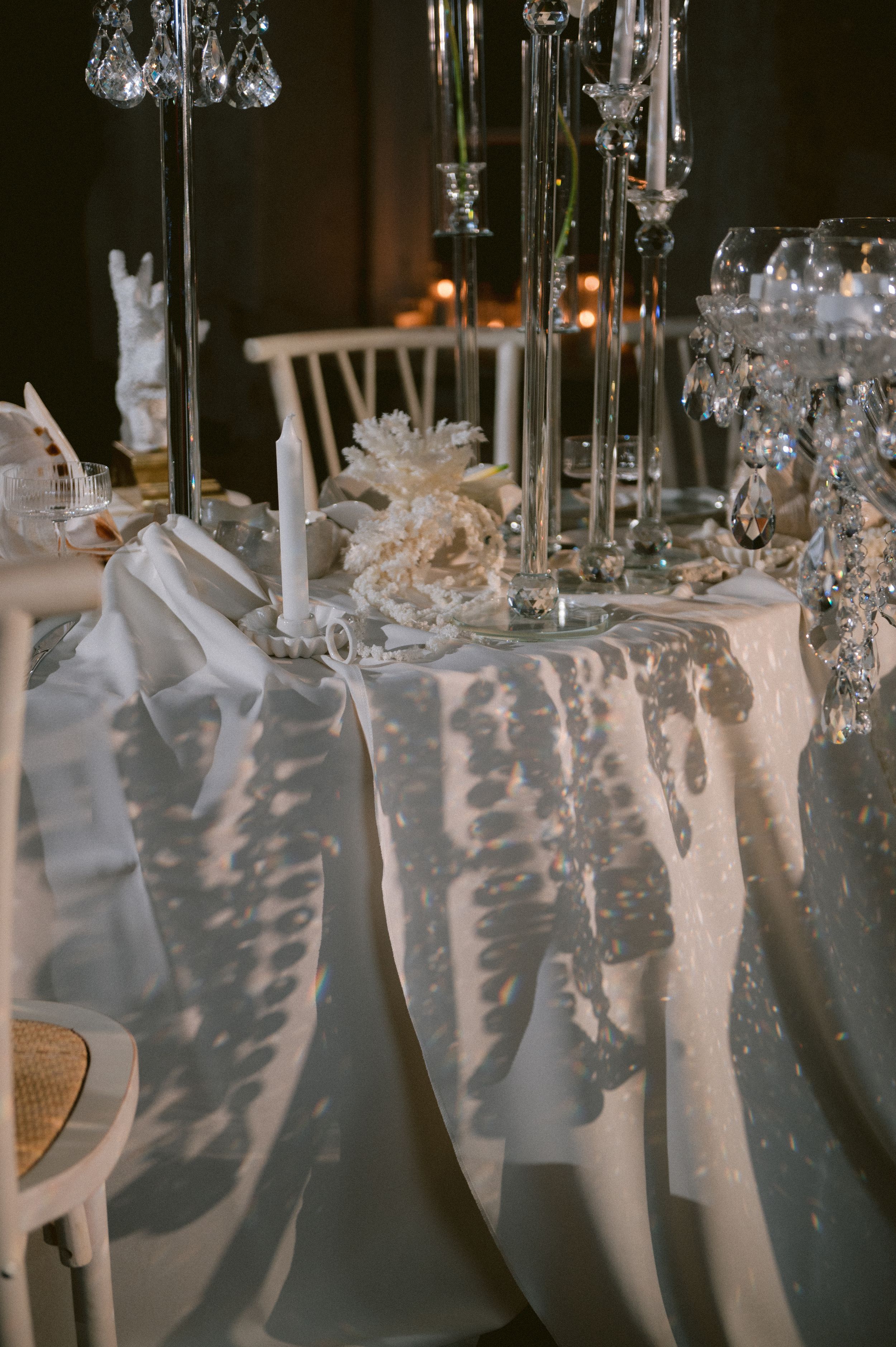 Elegant wedding reception table setting with crystal candelabras casting dramatic shadows on white tablecloth decor.