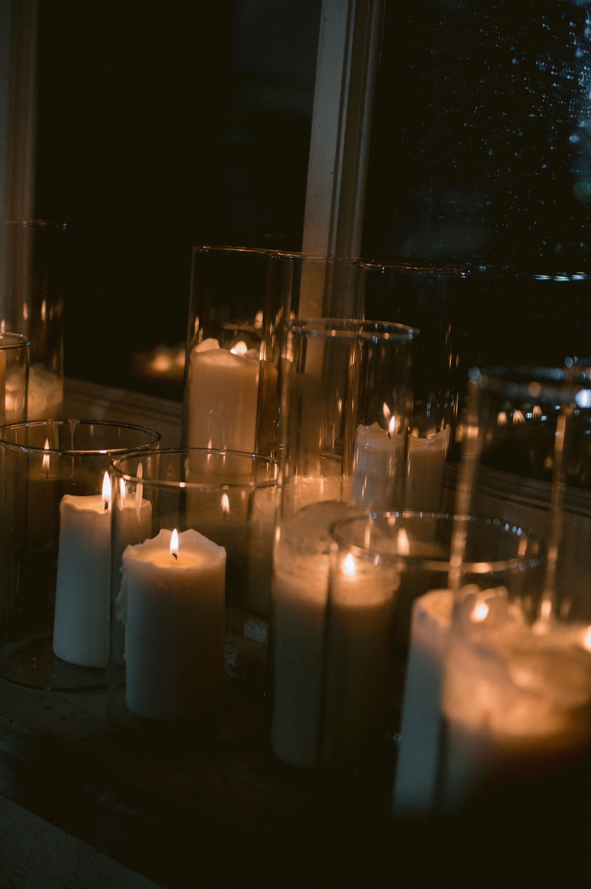 Multiple glowing white pillar candles create a warm, romantic atmosphere in glass holders at night.