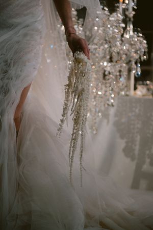 Crystal beads and ornaments sparkle against flowing white wedding dress fabric in an ethereal bridal detail shot.