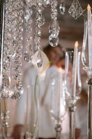 Crystal droplets hang from a chandelier with glowing candles creating an elegant, romantic atmosphere in soft focus.