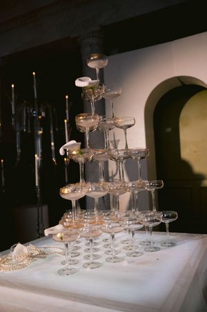 A tower of champagne glasses stacked in a pyramid formation on a white tablecloth with candlelight in the background.