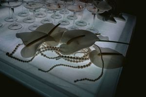 Wine glasses and pearl necklaces arranged on a white surface in dim lighting setting.