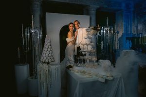A couple poses together at an elegant winter-themed wedding reception with icy blue lighting and white decorations.