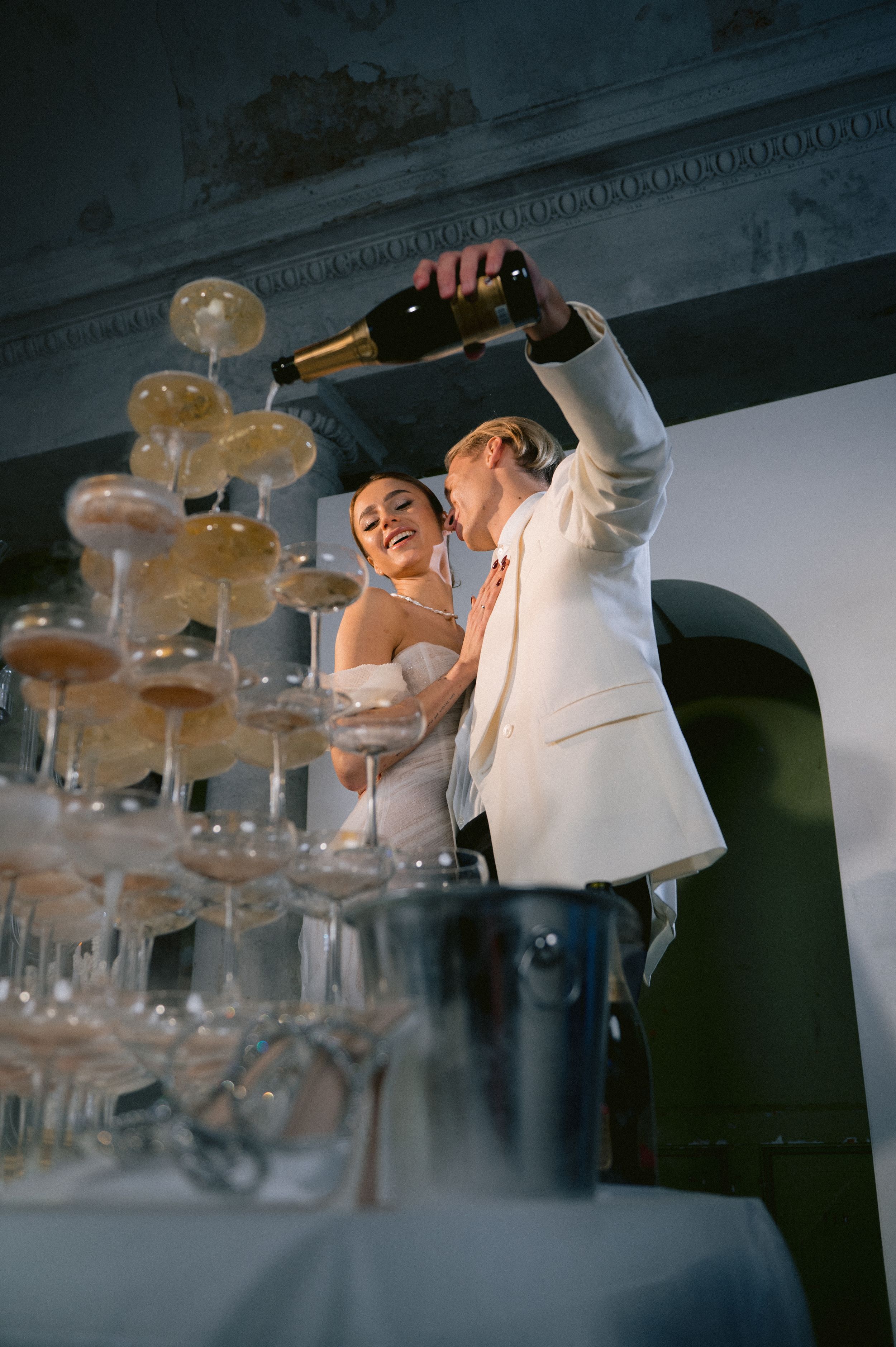 Newlyweds pour champagne into an elegant tower of crystal glasses at their wedding reception celebration.