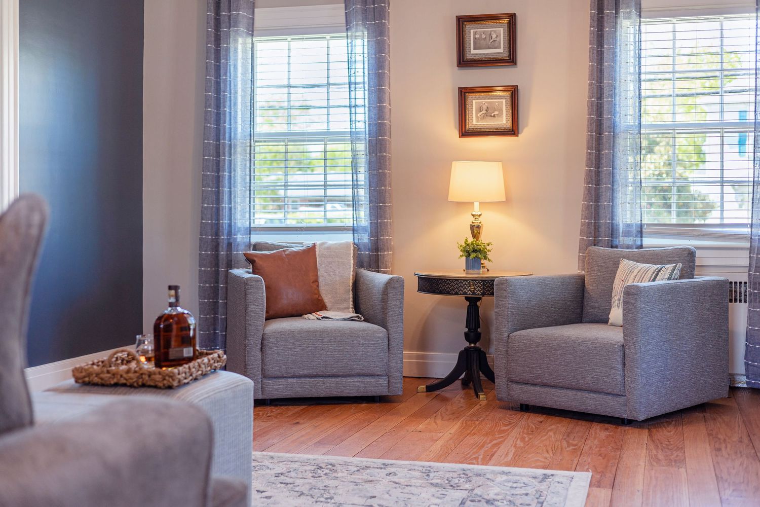 Cozy living room with two gray armchairs, blue curtains, and warm lighting from a table lamp.