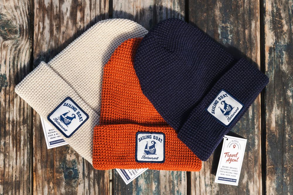 A collection of orange and navy blue knit winter beanies with tags displayed against a rustic wooden background.