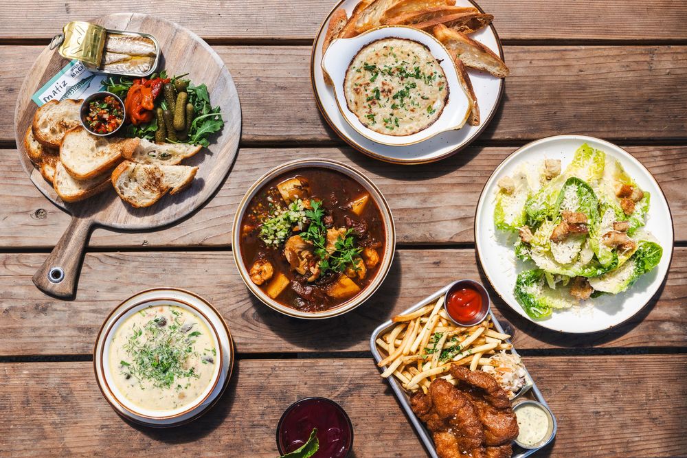 Overhead view of various restaurant dishes including soups, salads, and entrees arranged on a rustic wooden table.