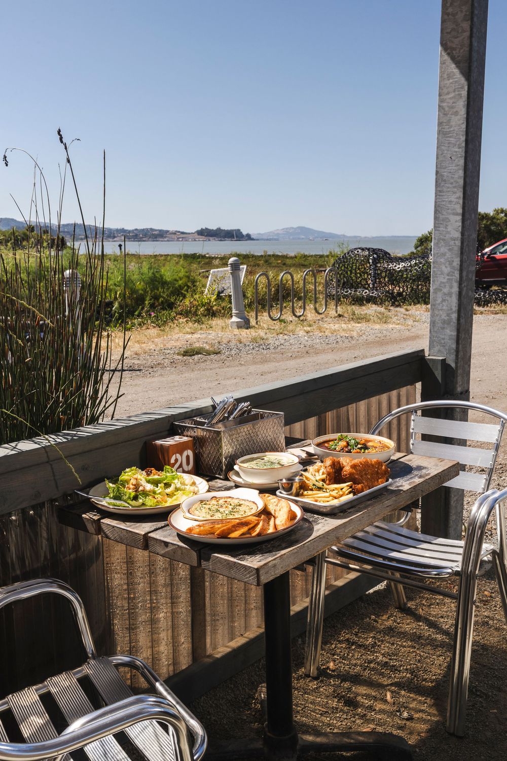 Outdoor buffet table setup with food dishes against a scenic rural landscape and mountains in the background.