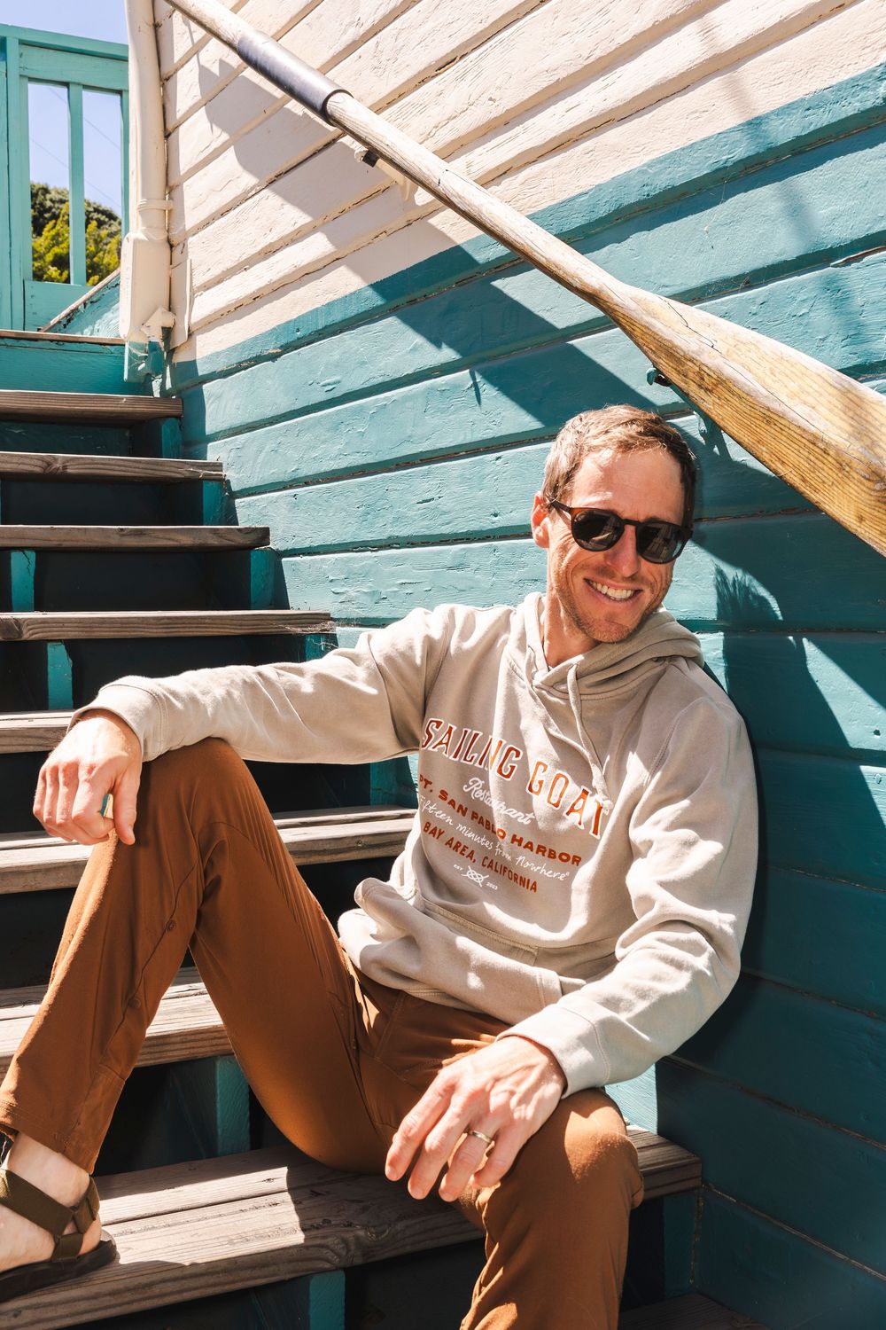 Person in sunglasses and casual attire relaxes on wooden bleacher steps in sunlit outdoor setting.