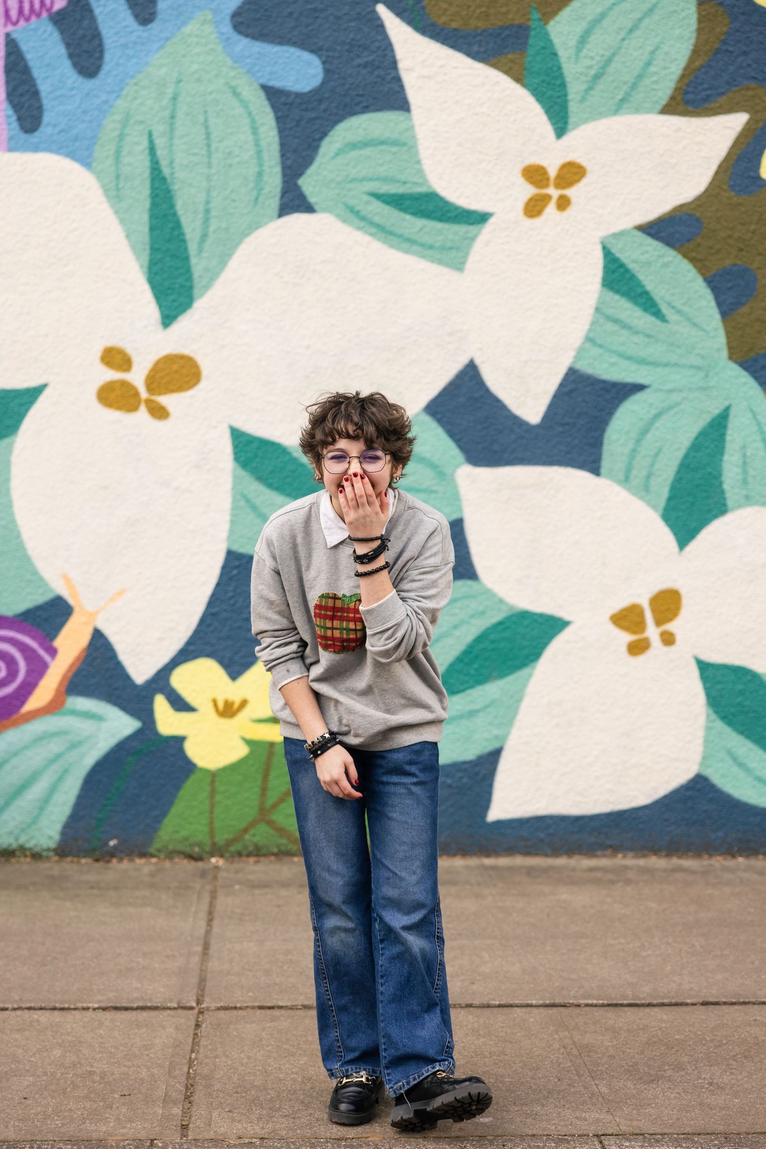 A candid moment against a colorful floral mural with white blossoms and mint green leaves on a wall.
