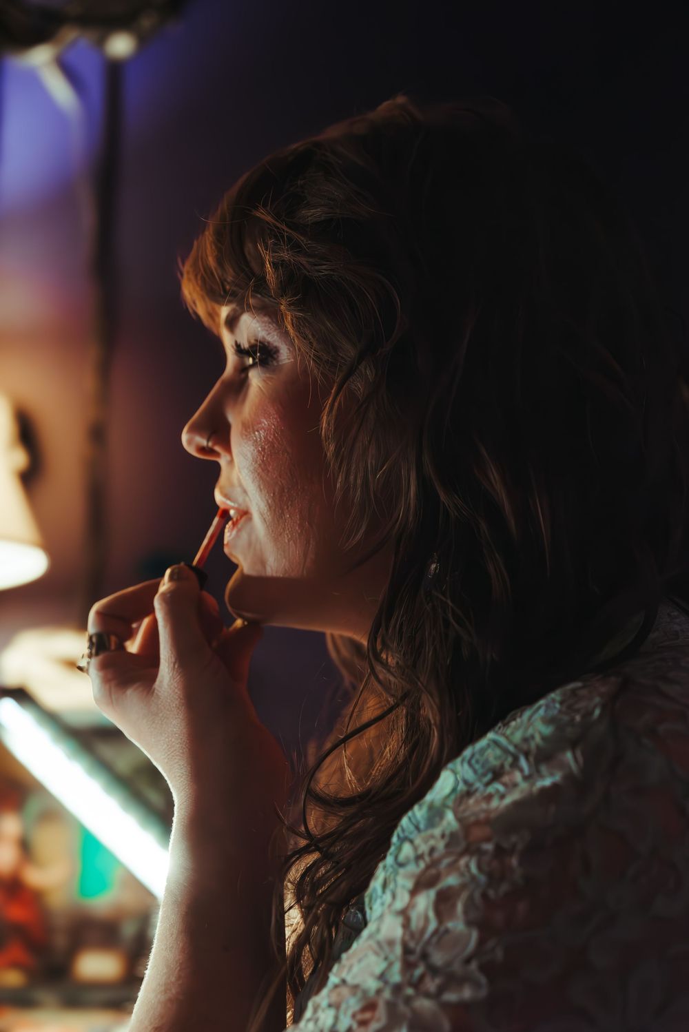 A side profile shot shows someone applying lipstick in warm ambient lighting with soft focus effects.