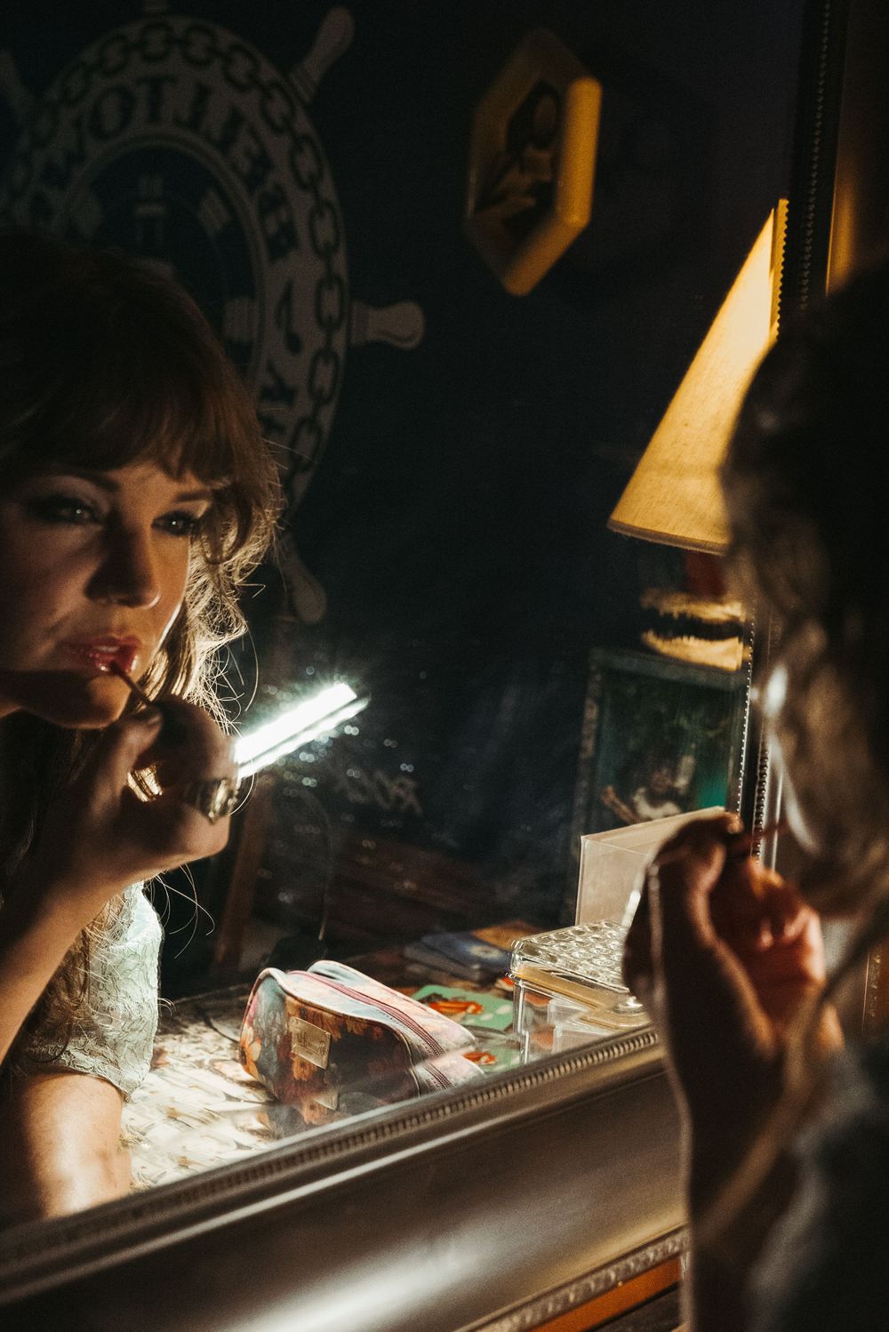 A moody portrait in dramatic lighting shows a reflection in a mirror with vintage decor.