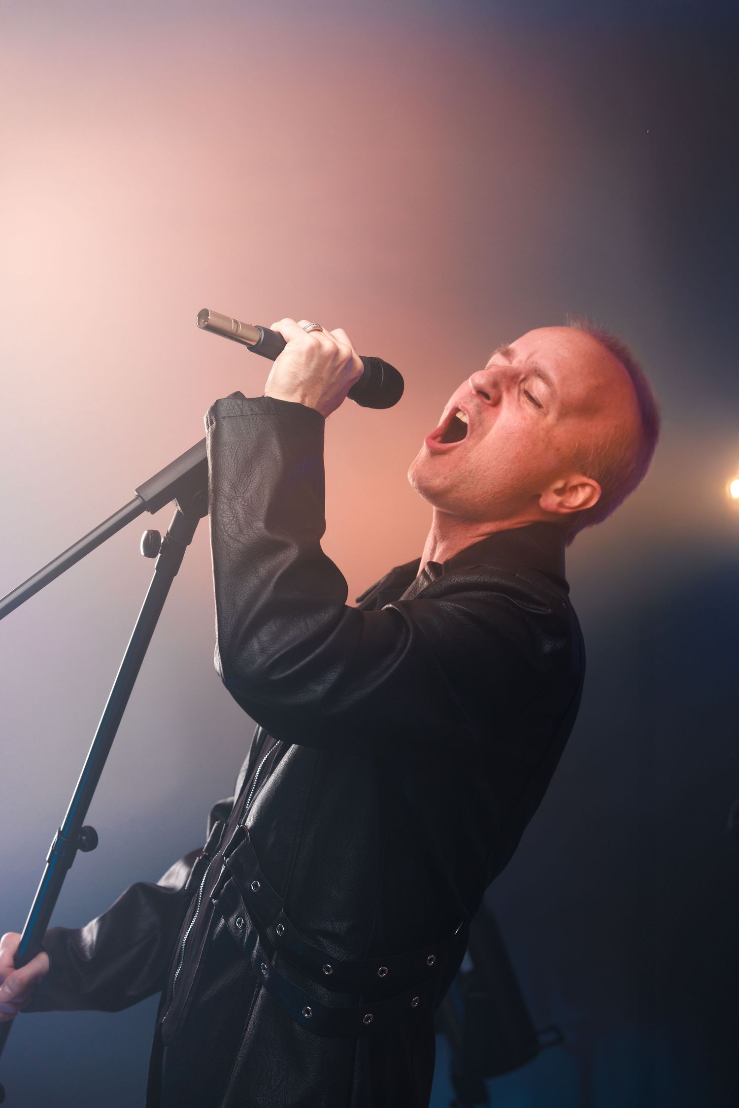 Singer performs passionately on stage with microphone in dramatic lighting.