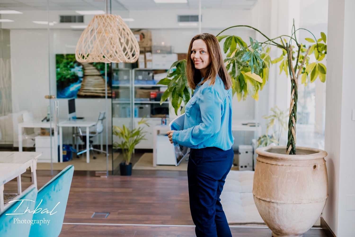 A businesswoman in a soft blue shirt turns toward the camera while walking through her office.
