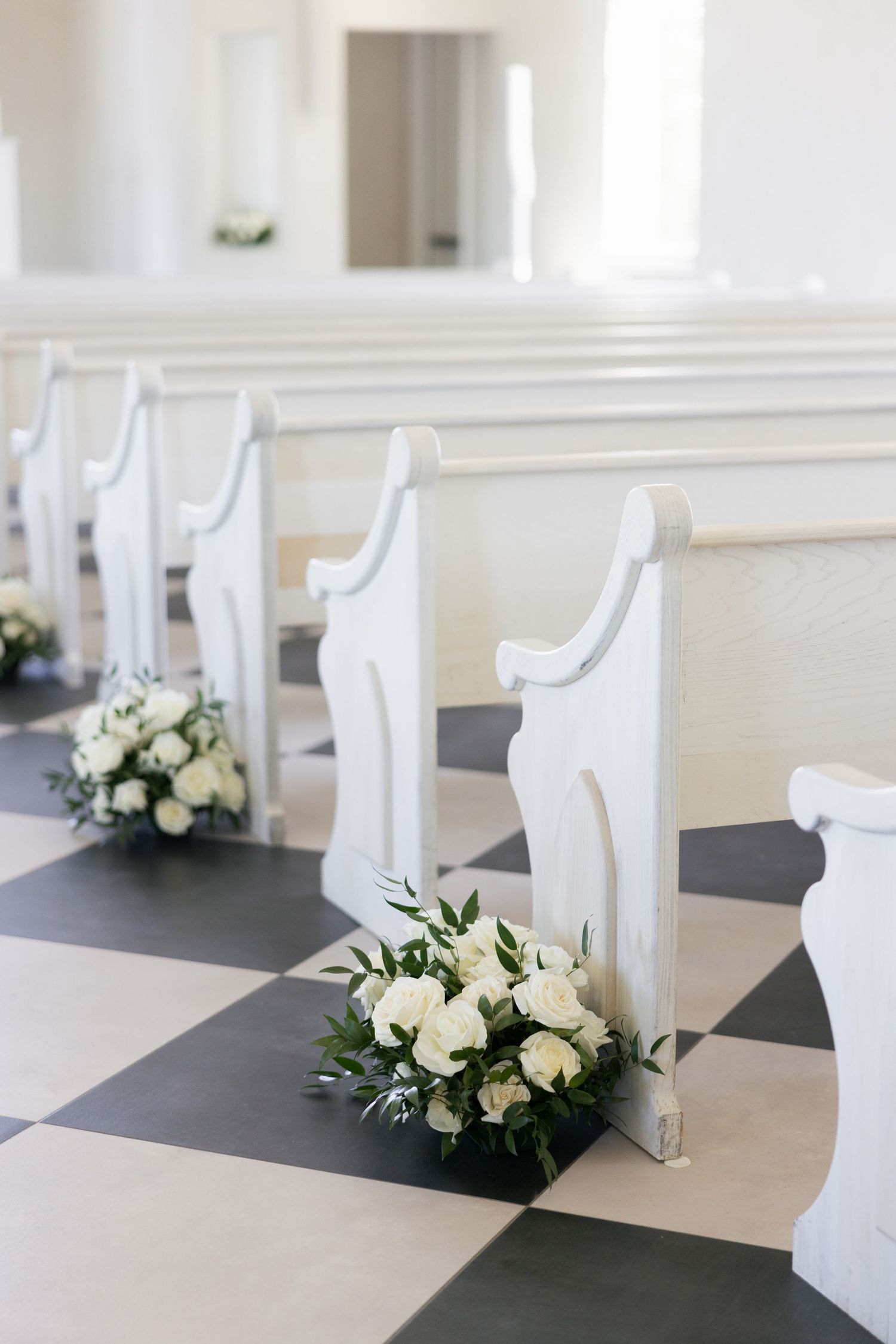 White floral centerpieces line a minimalist wedding venue reception table with classic white chairs.