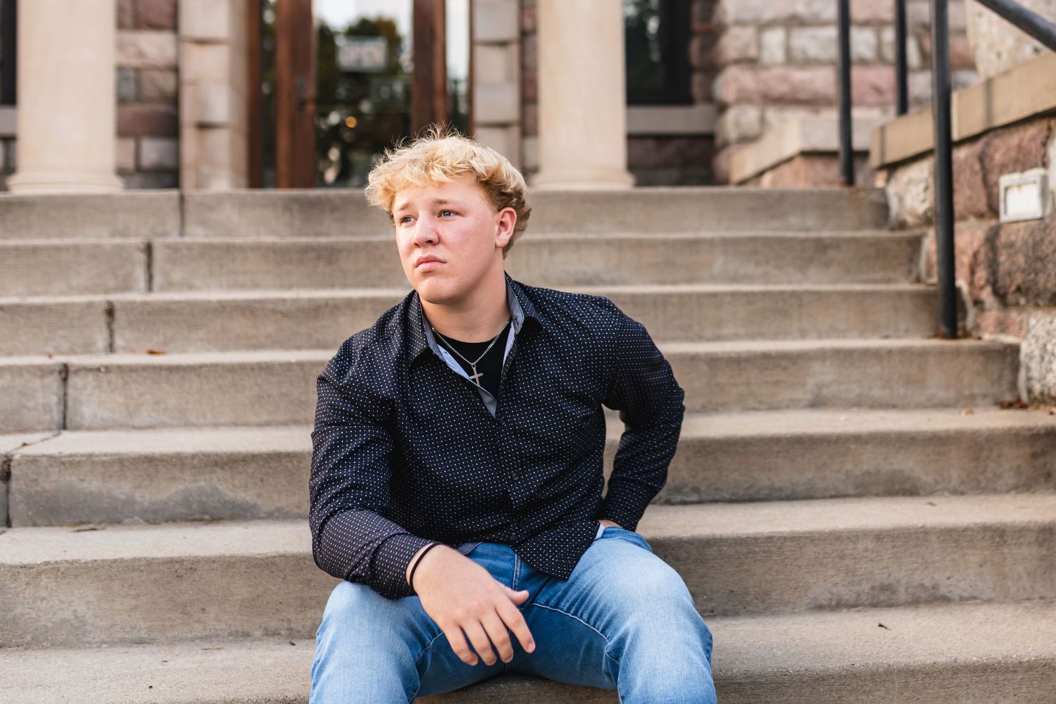 Portrait of a senior boy looking off into the distance while sitting on limestone steps.