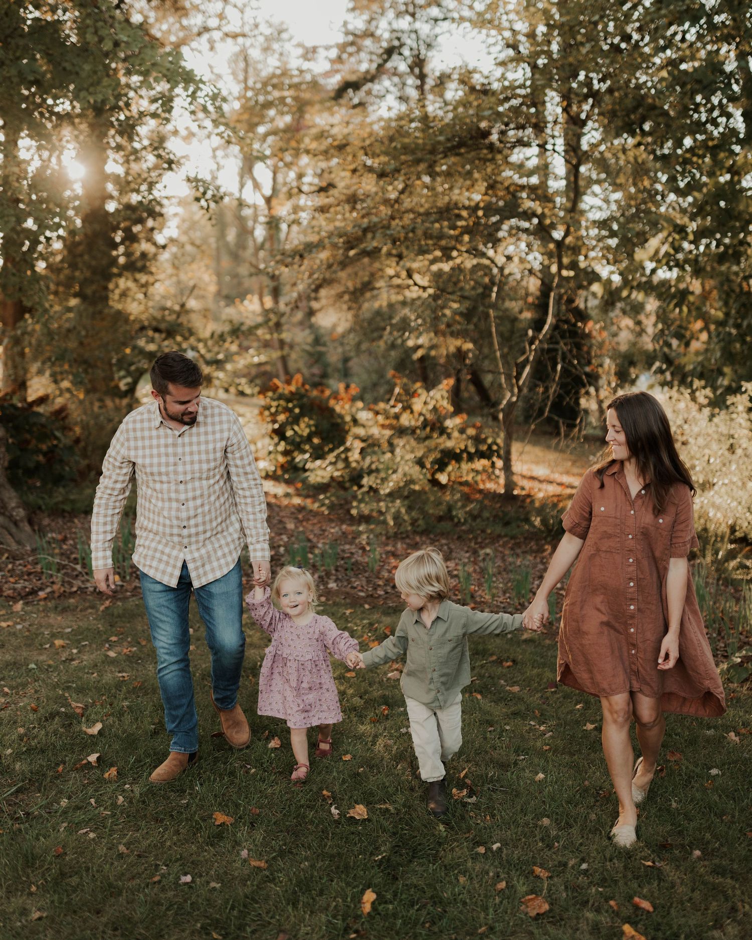 A family shares a joyful moment together in golden autumn sunlight among trees.