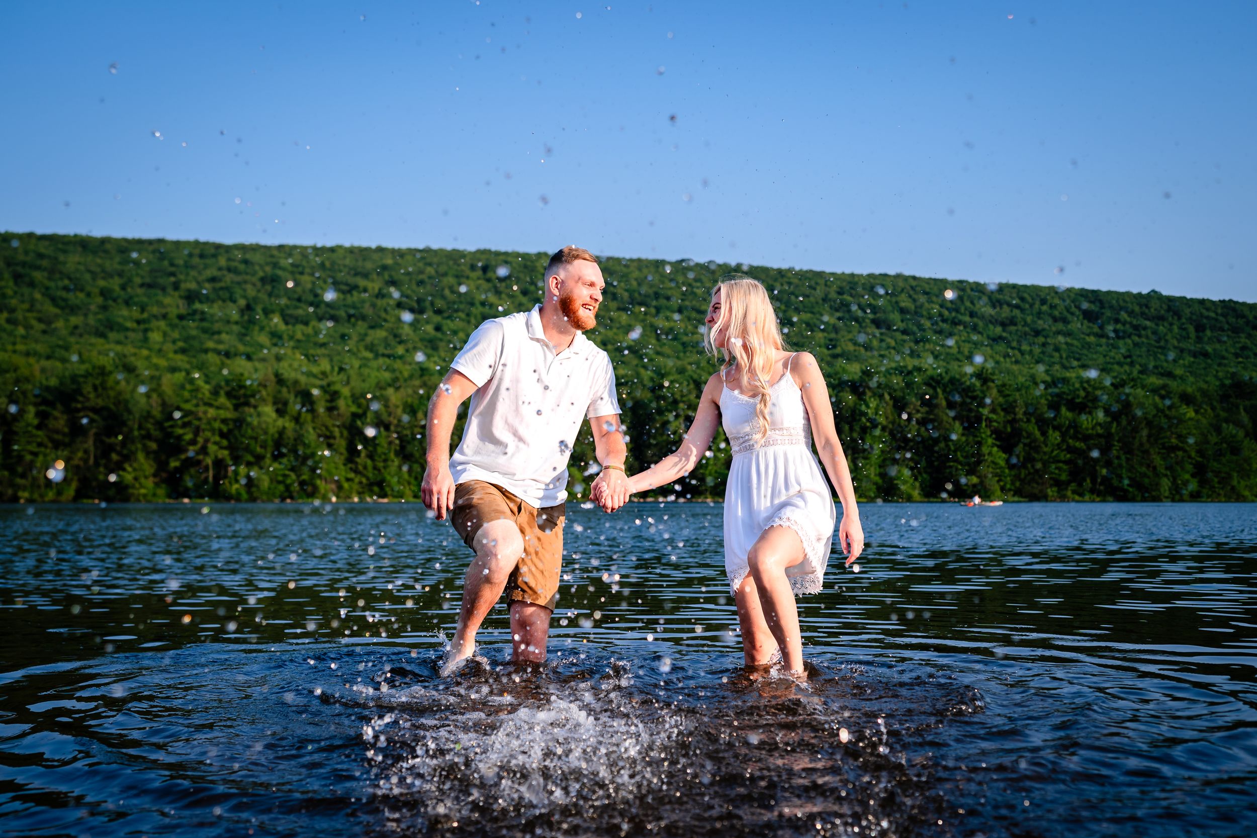 Playful couple splashing in lake water on sunny summer day.