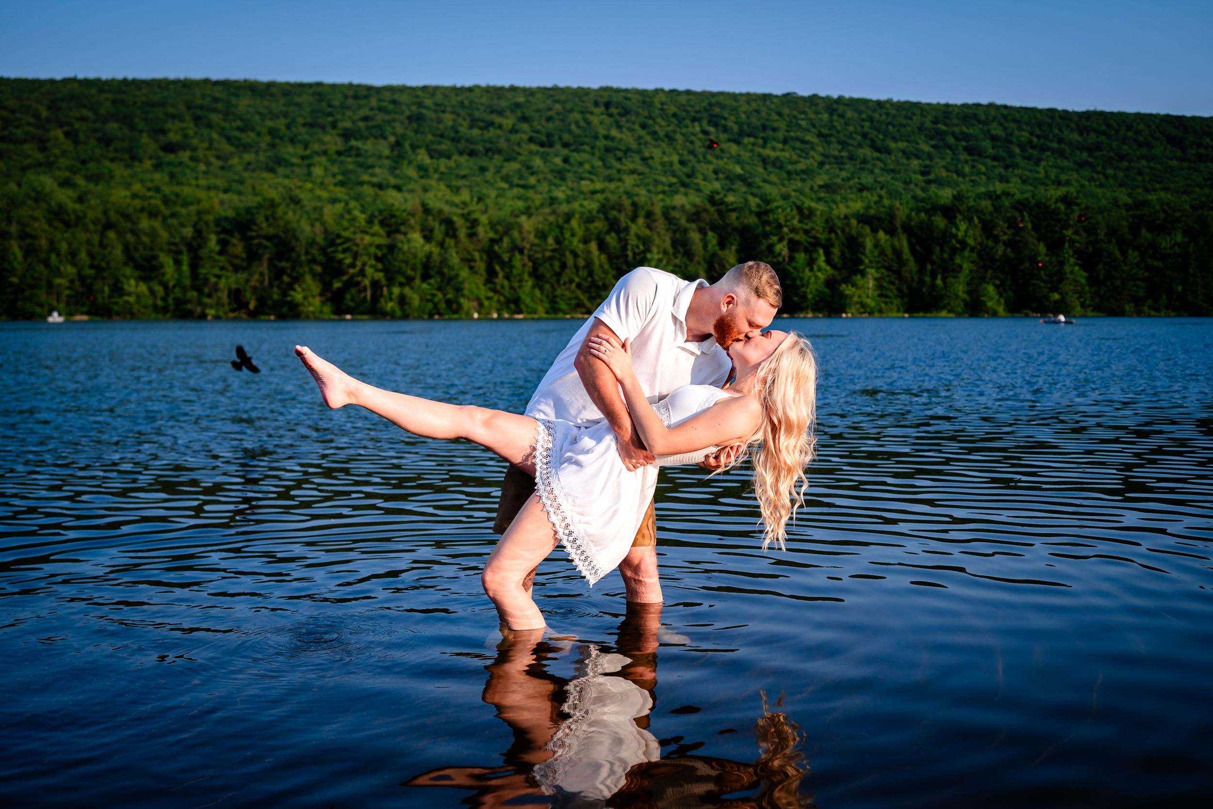 Couple shares romantic moments in a lake with lush green forest backdrop during a summer photoshoot.