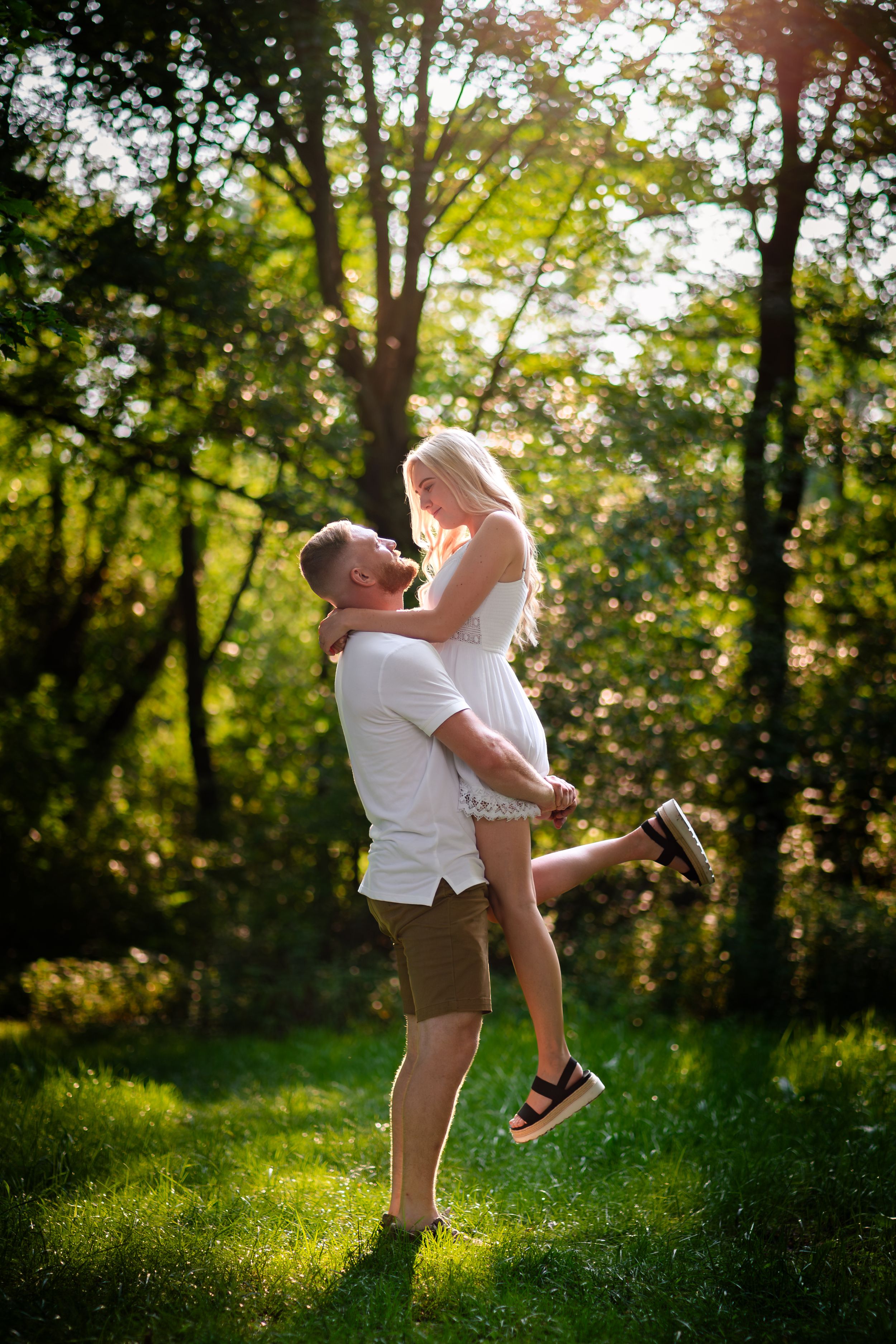 Playful outdoor photoshoot with couple in white clothing dancing and twirling in a sunlit forest.
