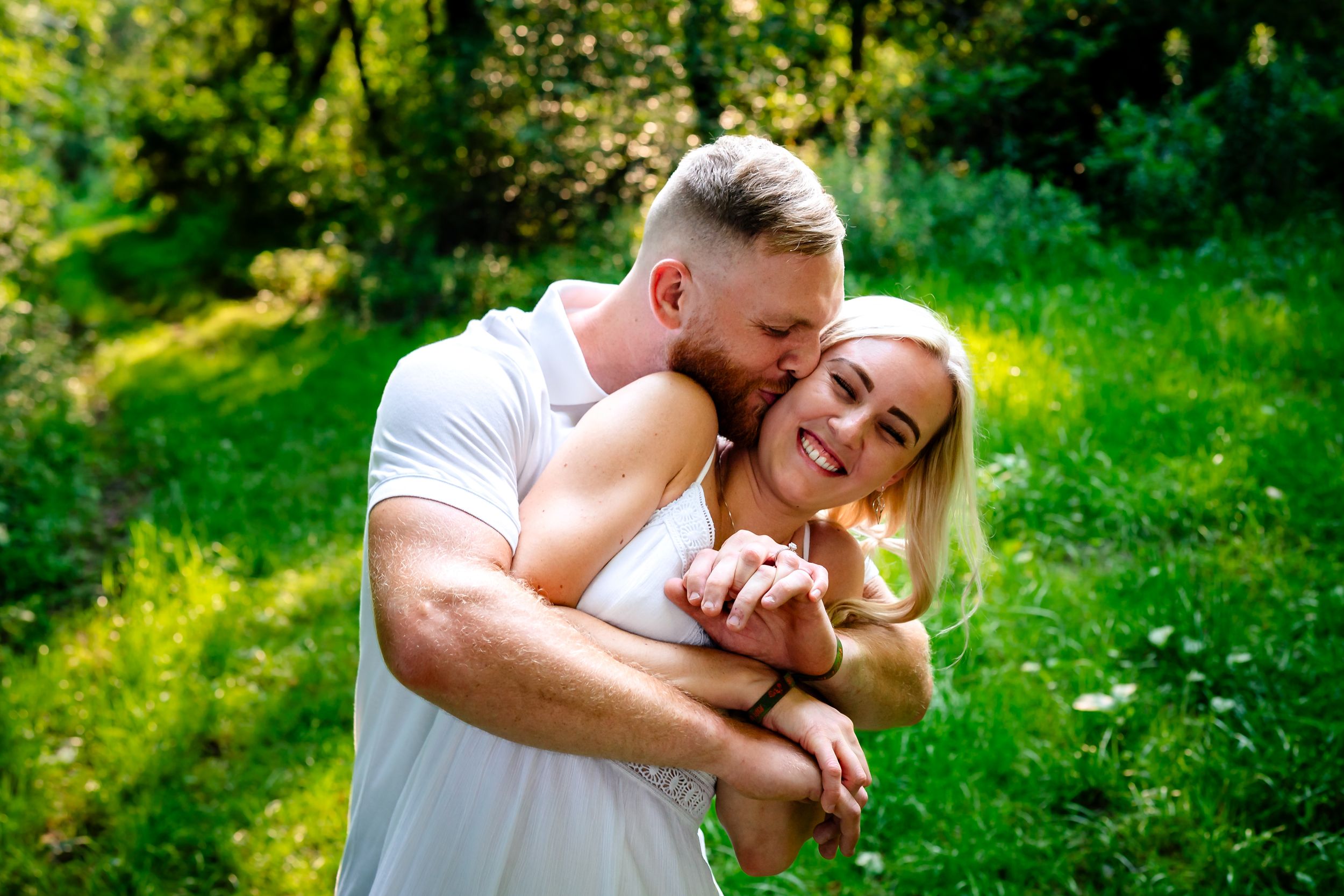 Candid moments captured between couple during outdoor summer photo session in vibrant greenery.
