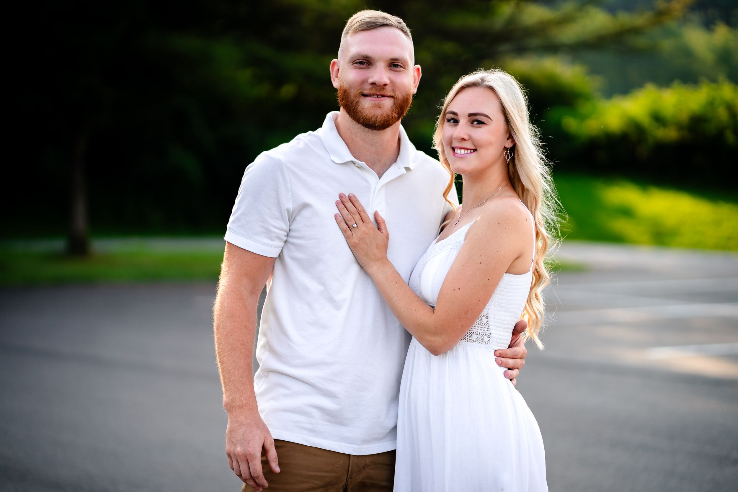 Romantic couple in white outfits embracing during golden hour photo session in a lush outdoor setting.