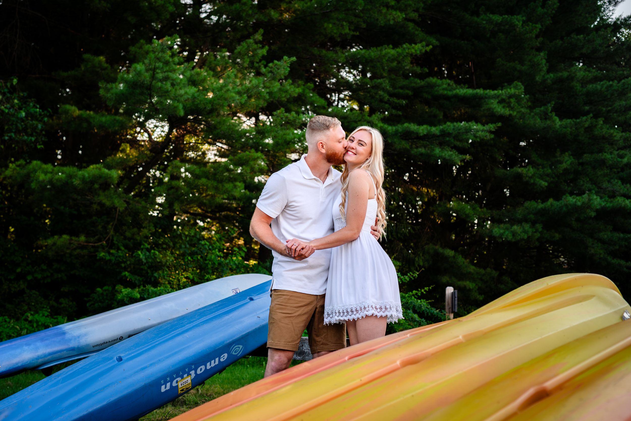 Couple posing near colorful canoes by a serene lake during engagement photography session.