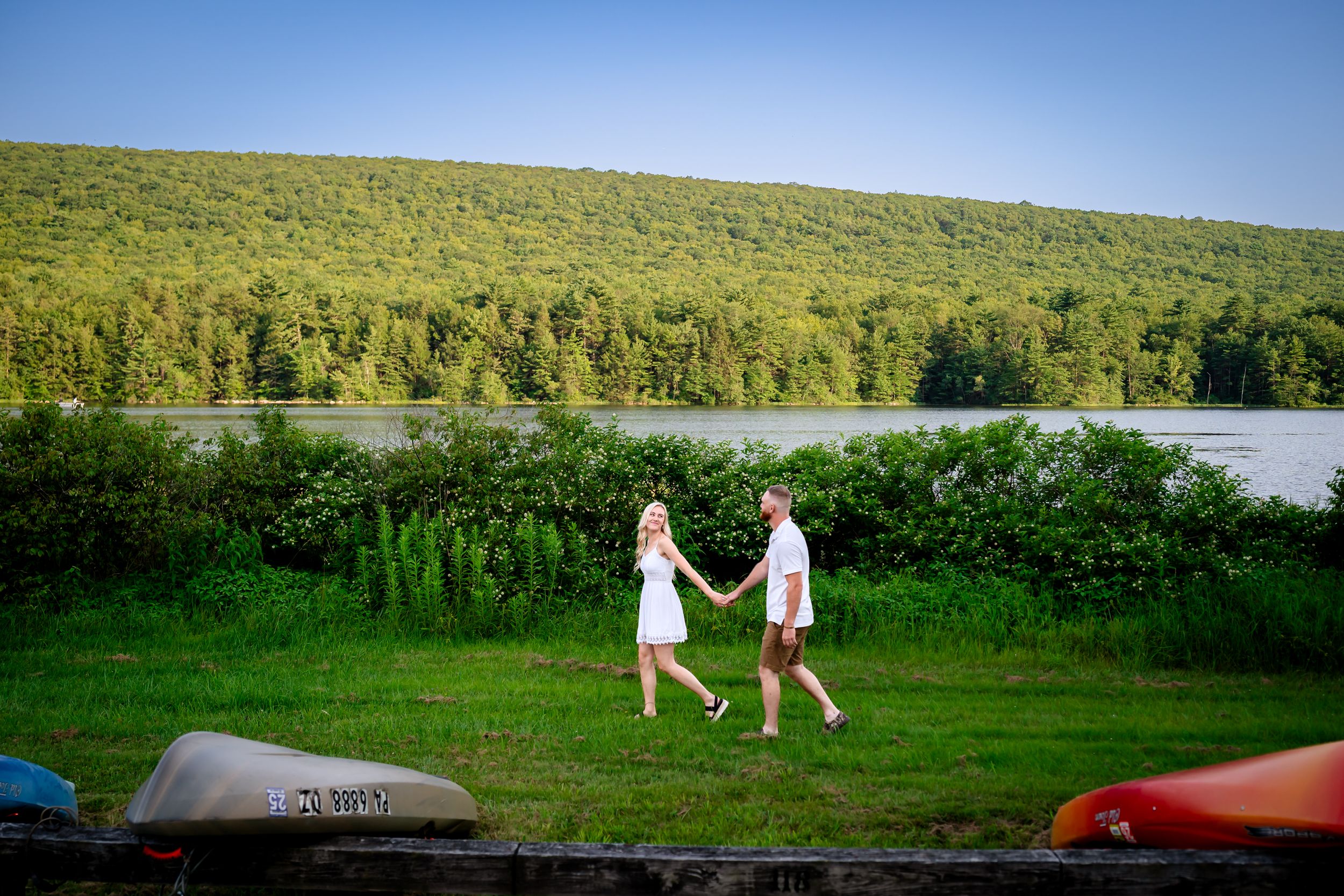 Panoramic landscape view of rolling hills and lake with couple walking in the distance.