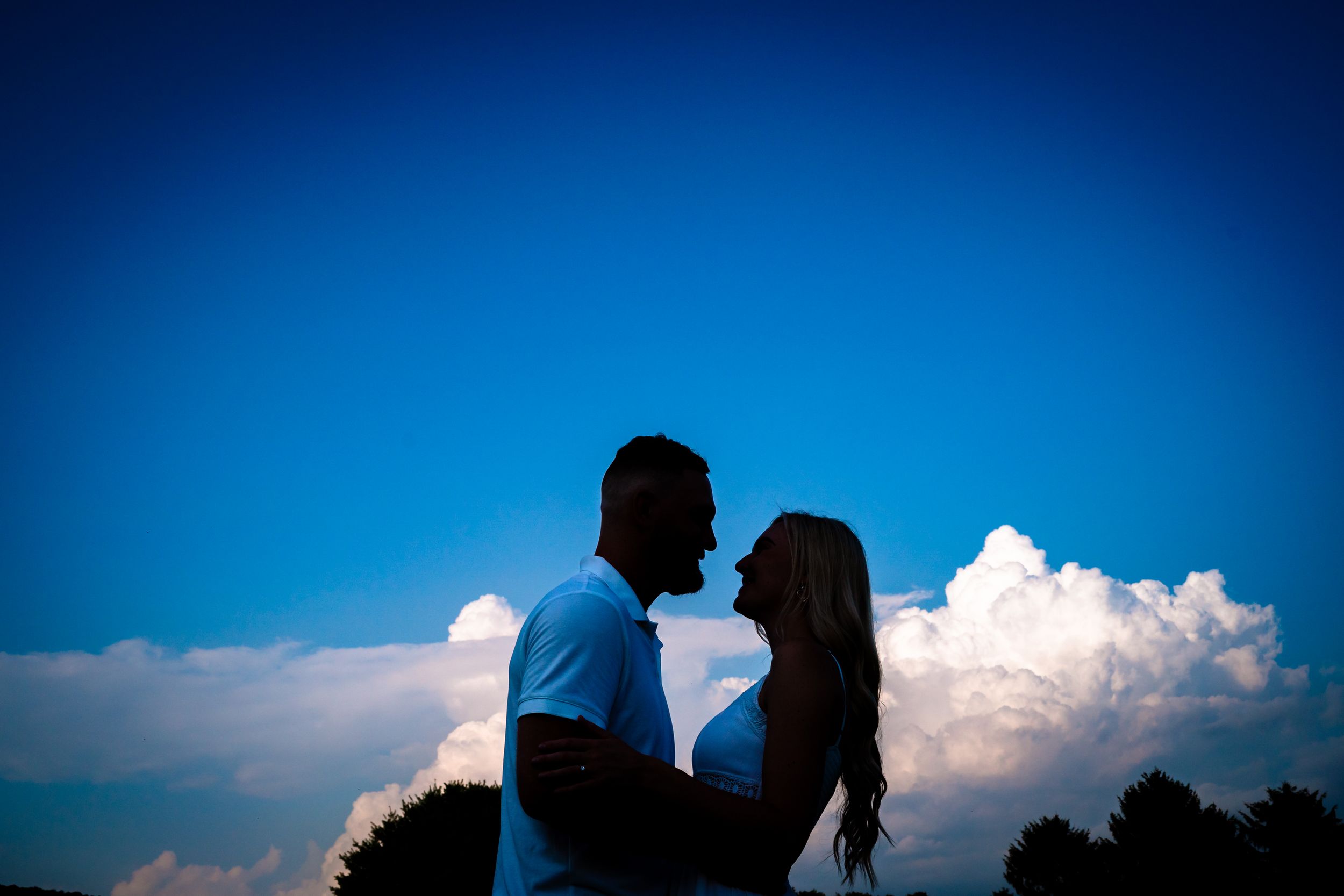 Silhouettes of couple against dramatic blue sky with white puffy clouds.