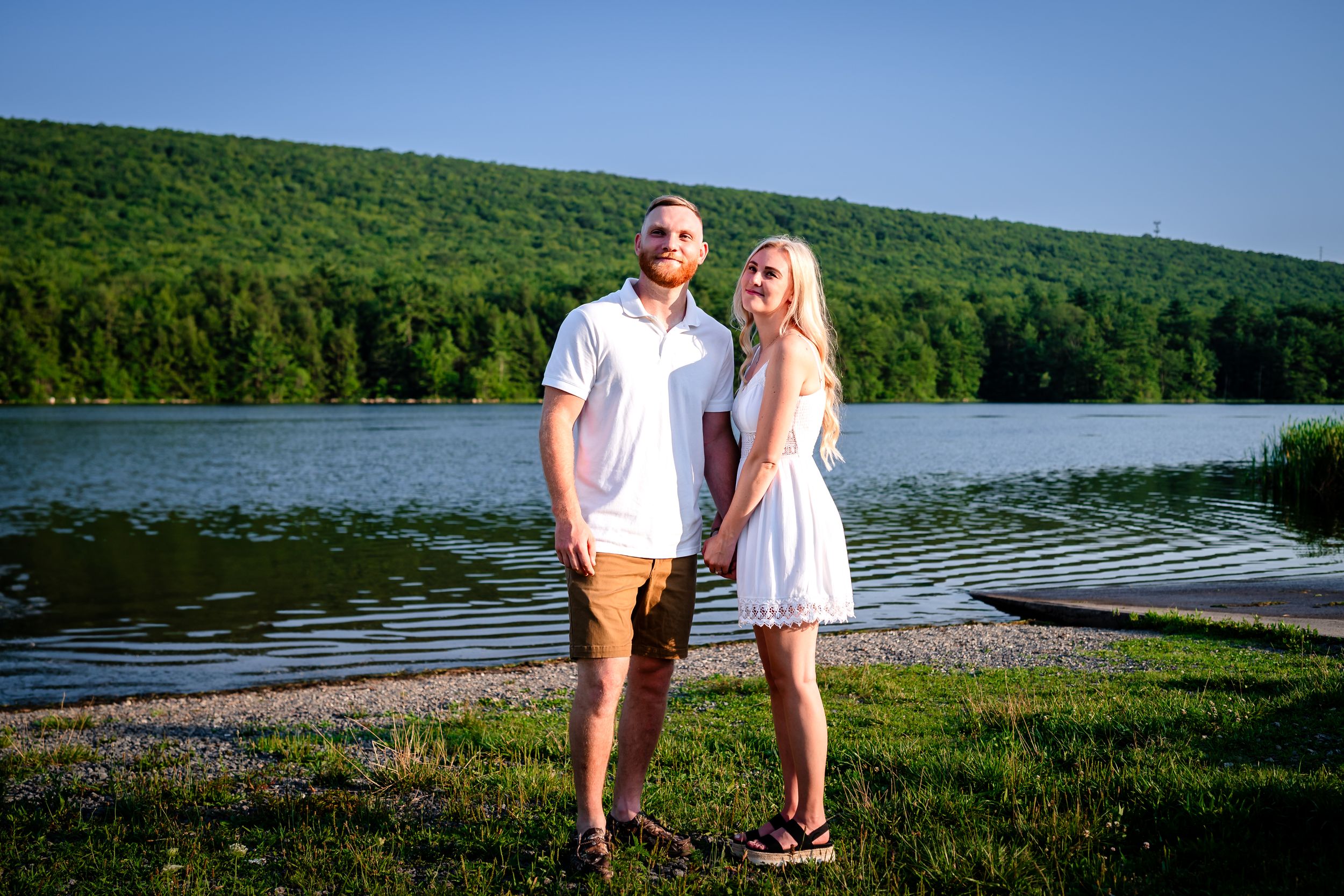 Couple walking along scenic lakeside path with mountains in background.