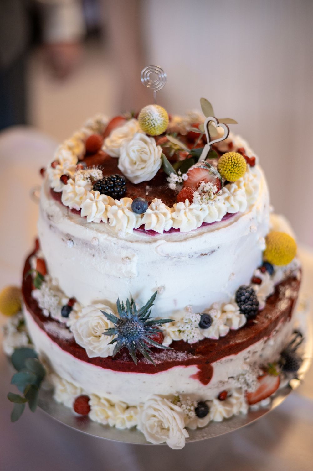 Eine zarte weiße Hochzeitstorte, dekoriert mit frischen Beeren, Feigen und essbaren Blüten.