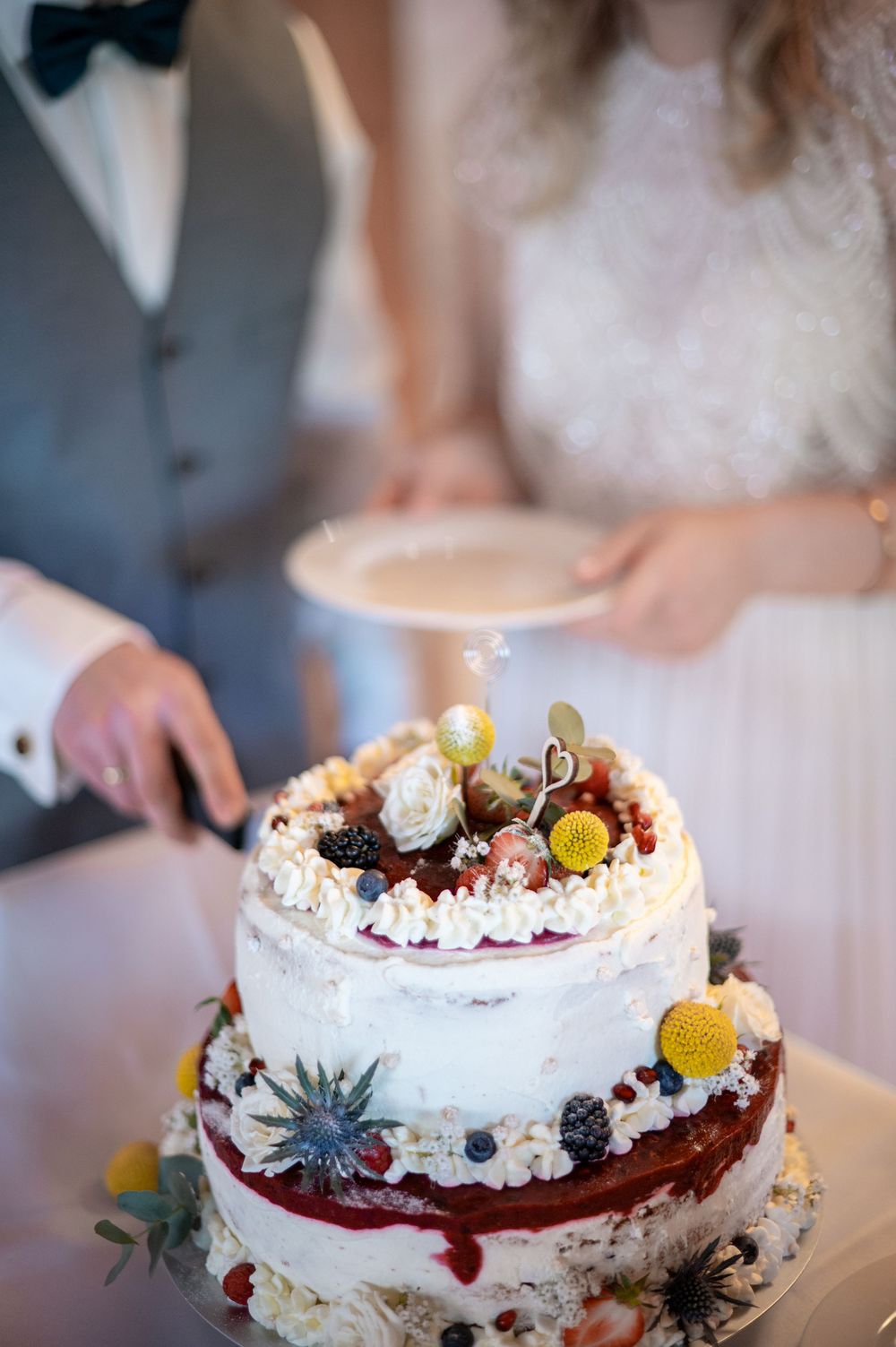 Eine zarte weiße Hochzeitstorte, dekoriert mit frischen Beeren, Feigen und essbaren Blüten.