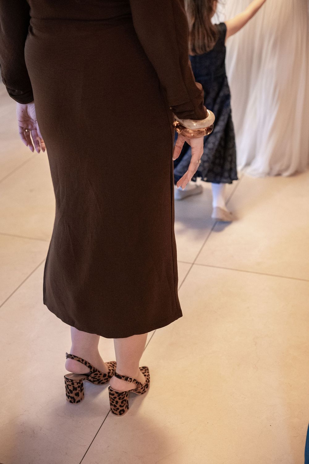 Detailaufnahme einer Gästin in braunem Kleid und Schuhen und Armreif mit Leomuster.