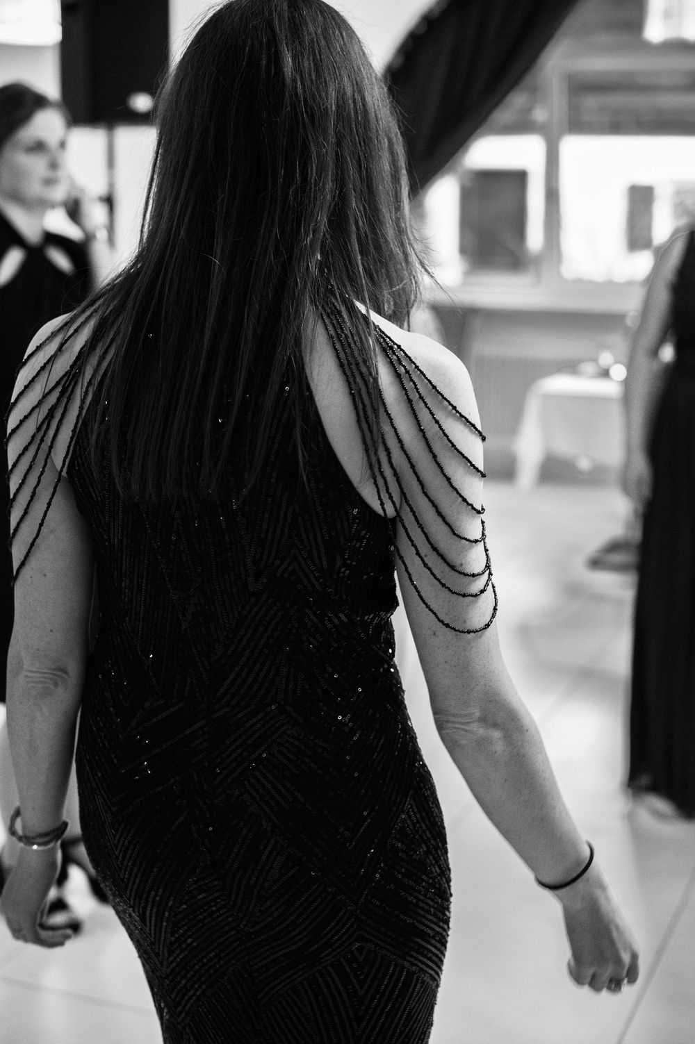 Schwarz-Weiß-Foto einer Frau, die den Rücken und die Schultern  in einem Kleid mit Perlenärmeln zeigt.