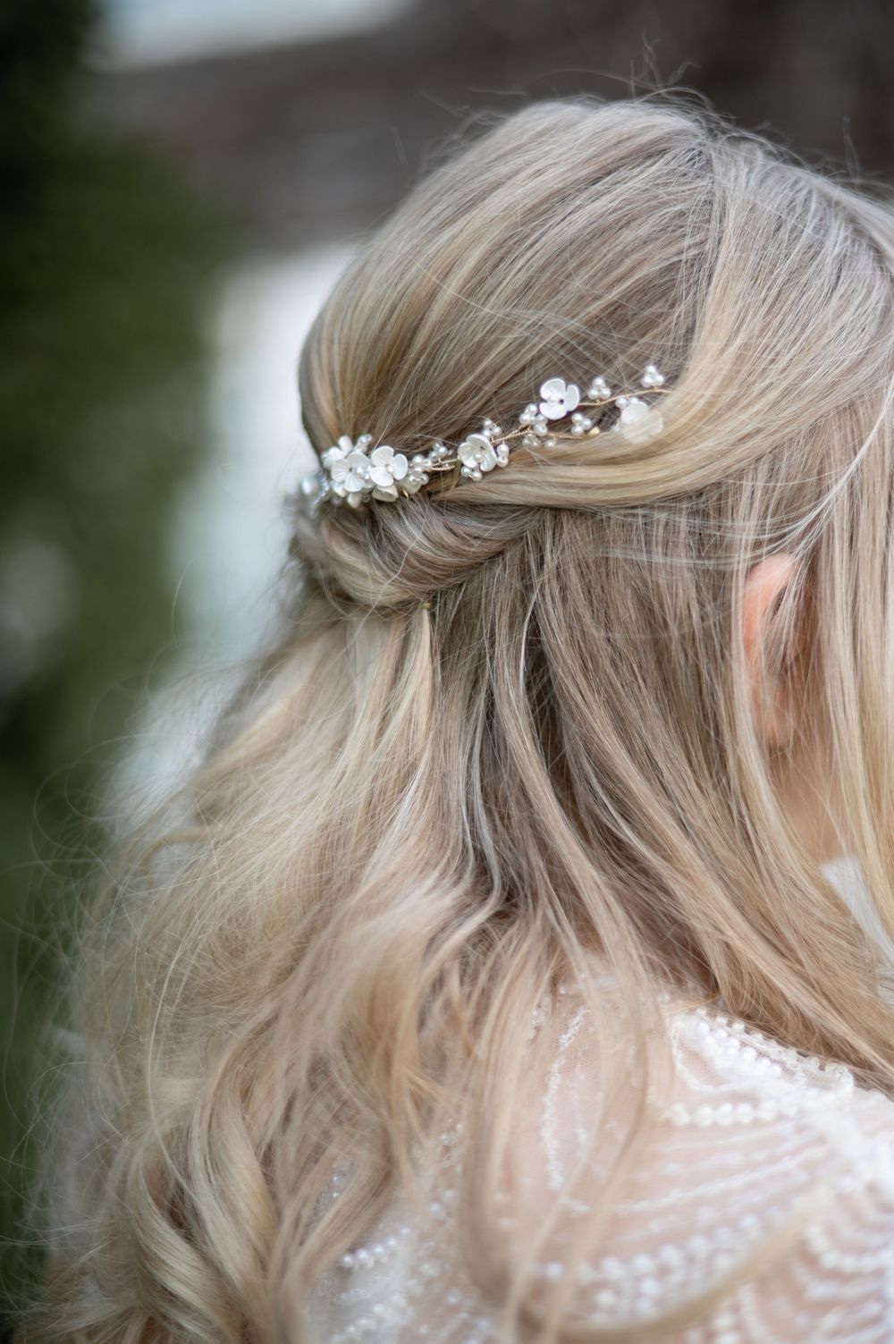 Zarter weißer Blumenhaarschmuck schmückt gestyltes blondes Haar mit weichen Wellen, perfekt für einen Brautlook.