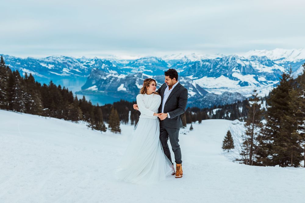 A couple poses for their wedding photos against a stunning backdrop of snow-covered mountain peaks and alpine scenery.