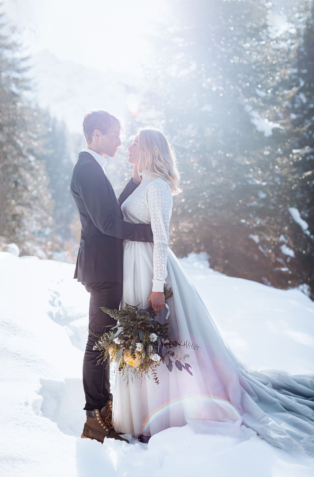 A romantic winter wedding photoshoot in a snowy forest with dreamy sunlight filtering through misty evergreen trees.