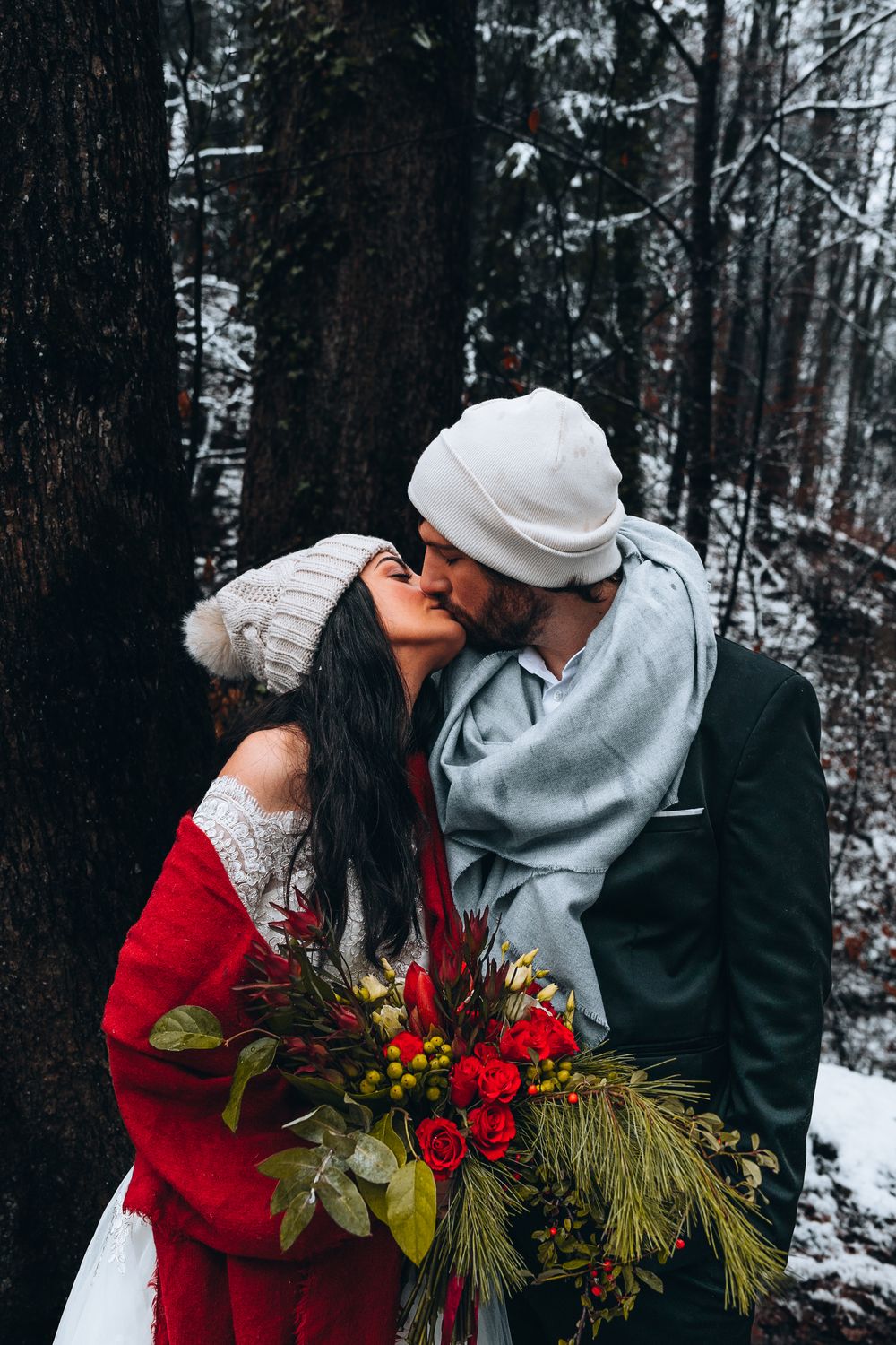 Romantic winter scene with red coat and bouquet of evergreens and berries in snowy forest setting.