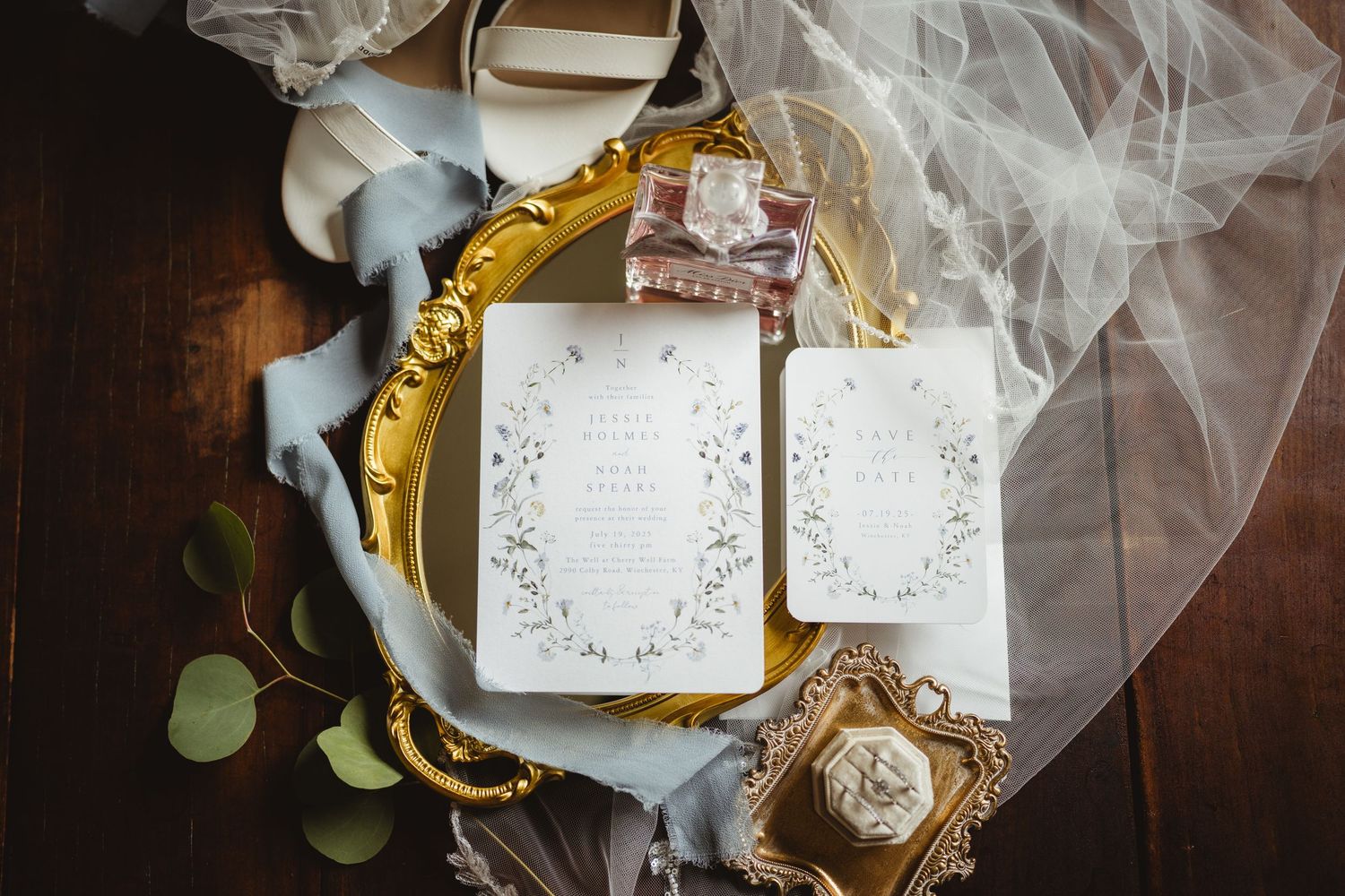 Ornate wedding invitation with floral design and veil on vintage gold frame displayed on dark wooden surface.