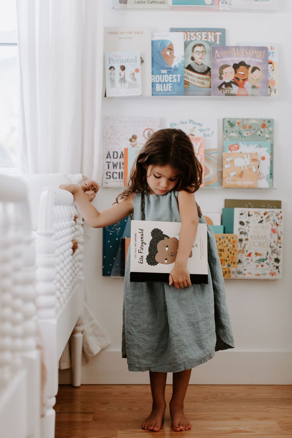 Children in gray dresses stand in a white room decorated with colorful artwork and books on display shelves.