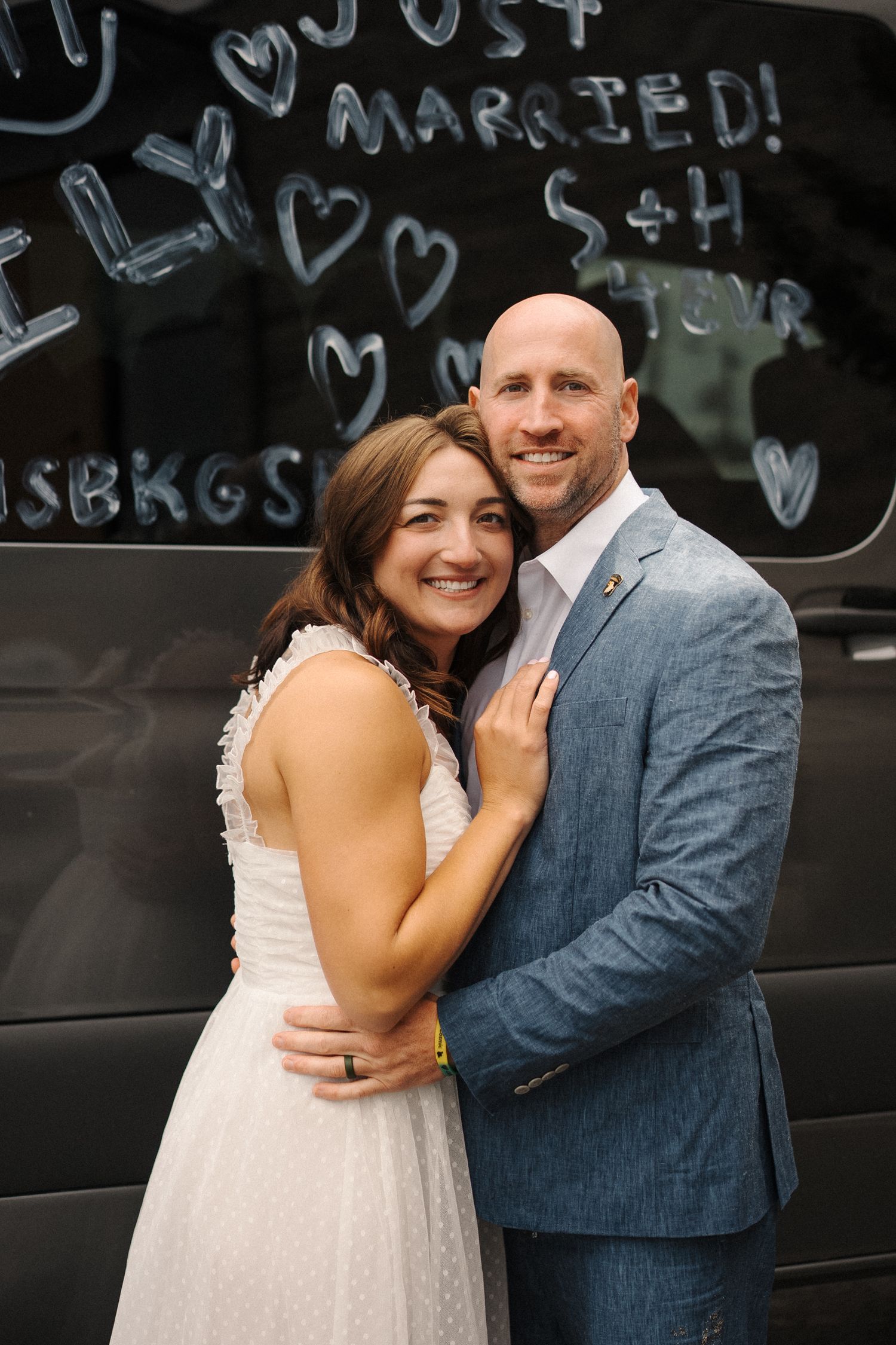 A newlywed couple embraces in front of a black wall with "Just Married" and hearts written in chalk.