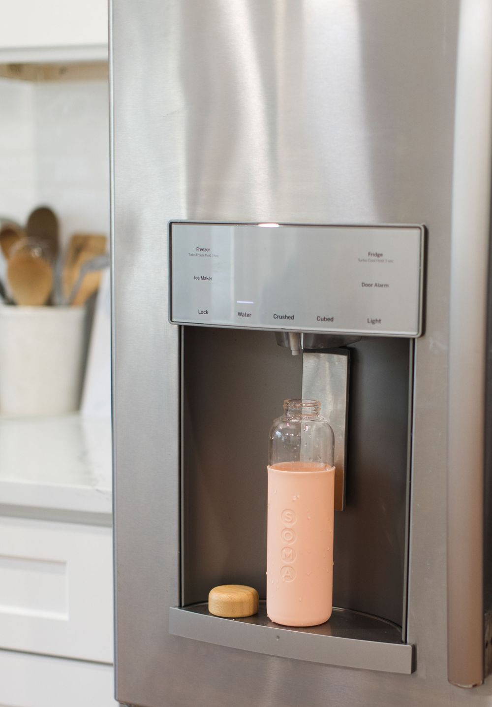 Stainless steel refrigerator with built-in water dispenser pouring pink liquid.